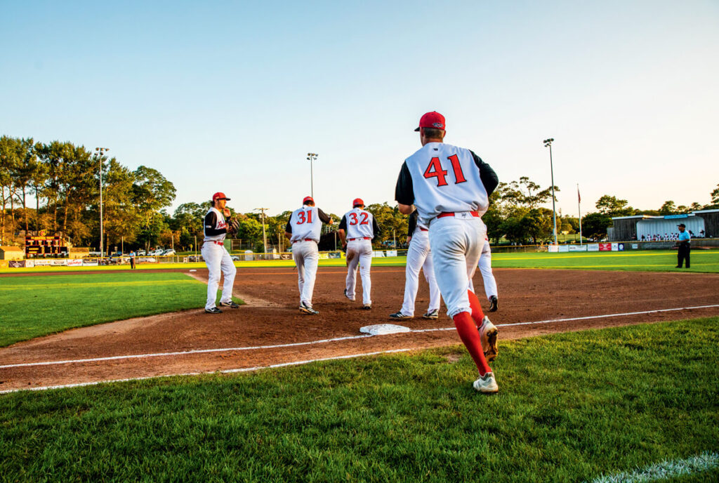 Baseball players in uniforms gather on the field at sunset, with player 41 running toward the group.