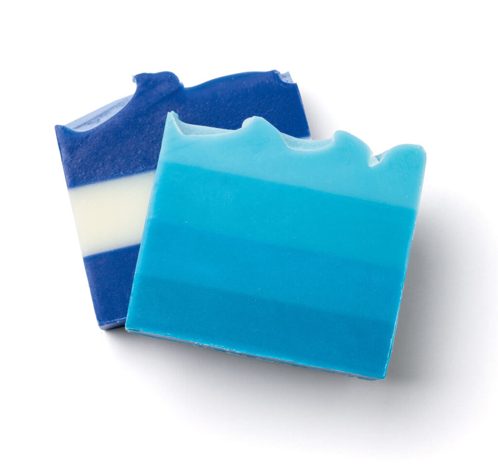 Two rectangular bars of blue layered soap with wavy tops, resembling ocean waves, on a white background.