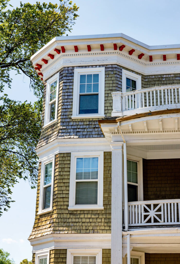 A three-story house with shingle siding, white trim, large windows, and a corner balcony.