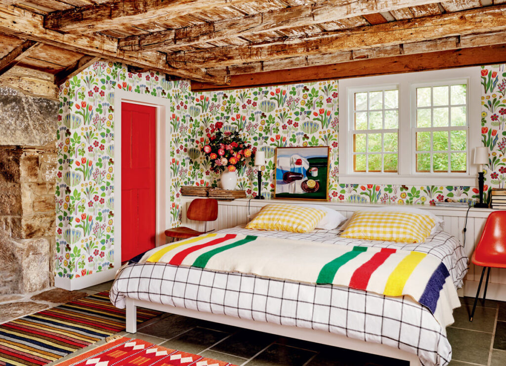 Cozy bedroom with floral wallpaper, wood ceiling, a striped bedspread, and red accents on the door and chairs.