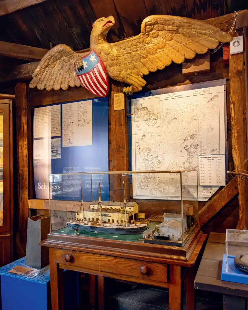 Model ship in a glass case beneath a large eagle sculpture with a US shield, in a maritime museum display.
