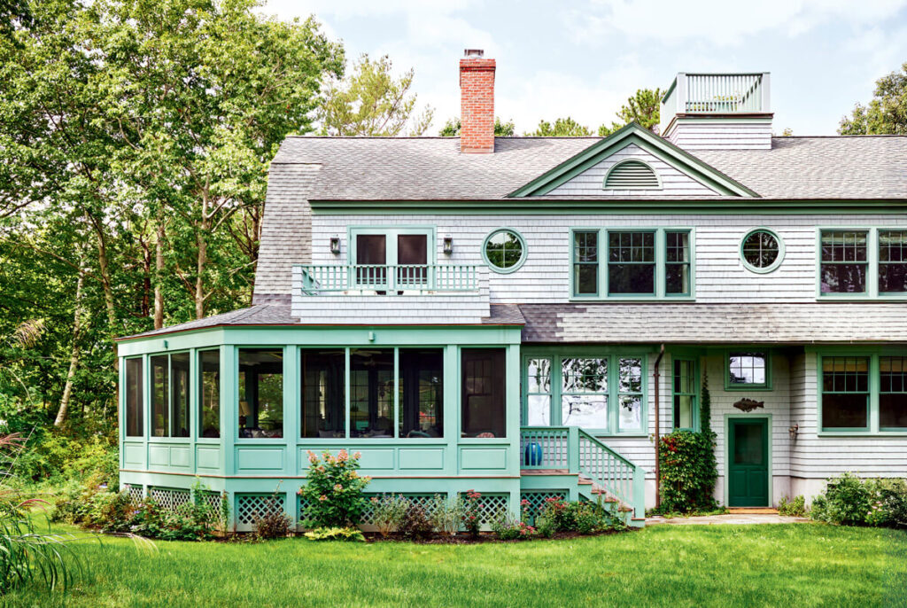 Large house with gray siding, green trim, screened porch, and lush green lawn surrounded by trees.
