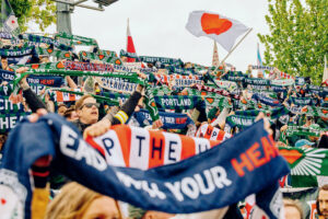 Soccer fans holding up colorful scarves and flags during a match, cheering in a packed stadium.