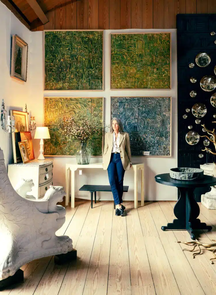 A woman stands in an art-filled room with abstract paintings, sculpture, and eclectic decor.