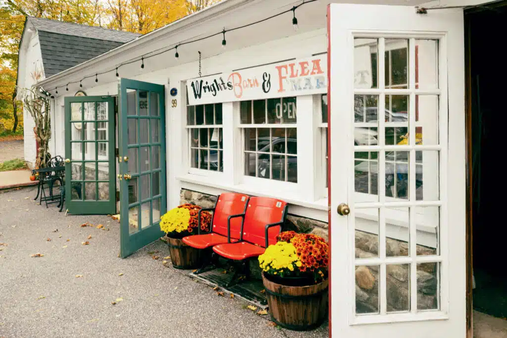 Guide to the Litchfield Hills. Red bench with potted yellow and red flowers outside a vintage shop with open doors.