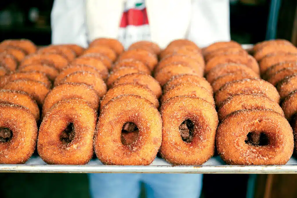 A person holds a tray filled with rows of sugar-coated donuts.