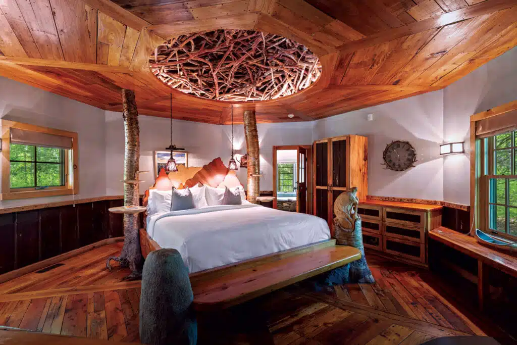 Rustic bedroom with wood accents, circular nest ceiling, large bed, windows, and tree-themed decor.