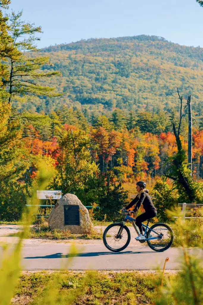 Fall Weekend in North Conway, New Hampshire. Person biking on a paved path with autumn trees and a mountain in the background.