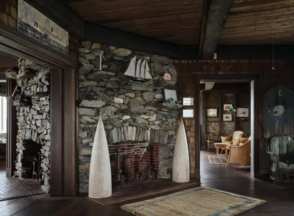 Rustic room with stone fireplace, nautical decor, wooden ceiling, wicker furniture, and framed wall art.