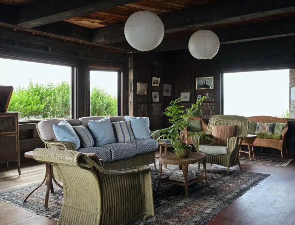 Cozy living room with wicker furniture, blue cushions, paper lanterns, and large windows with garden views.