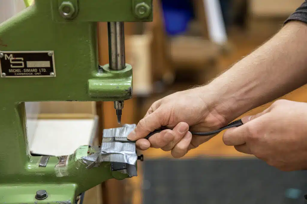Close-up of hands using a green press machine, with duct tape securing a small item under the press.