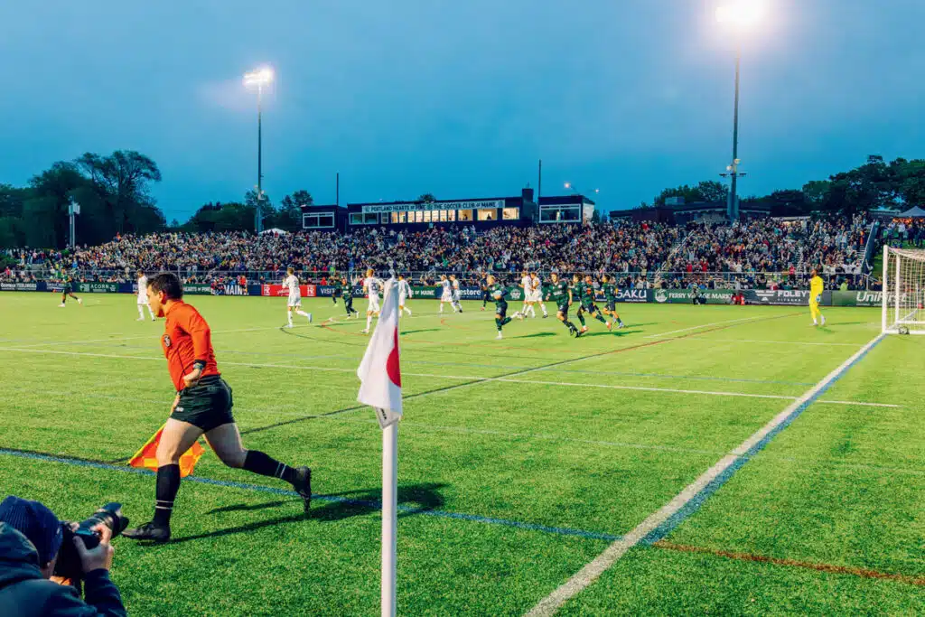 A soccer match in progress at a stadium with a large crowd and a referee running along the sideline.