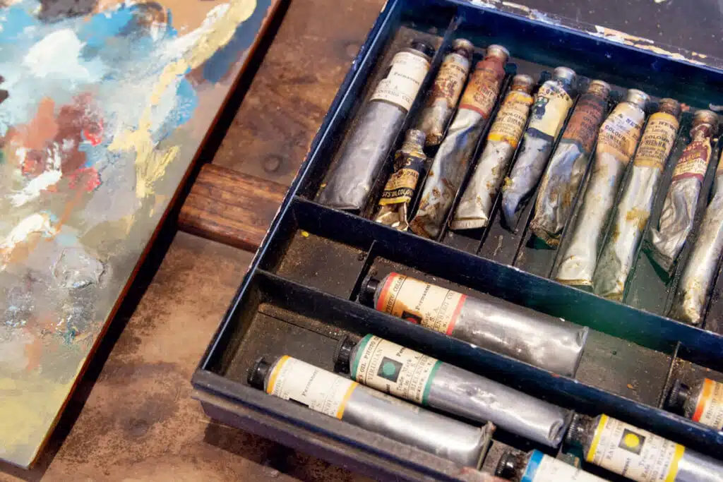 Winslow Homer's Studio in Scarborough, Maine. Open box of used paint tubes beside a colorful abstract painting on a wooden surface.