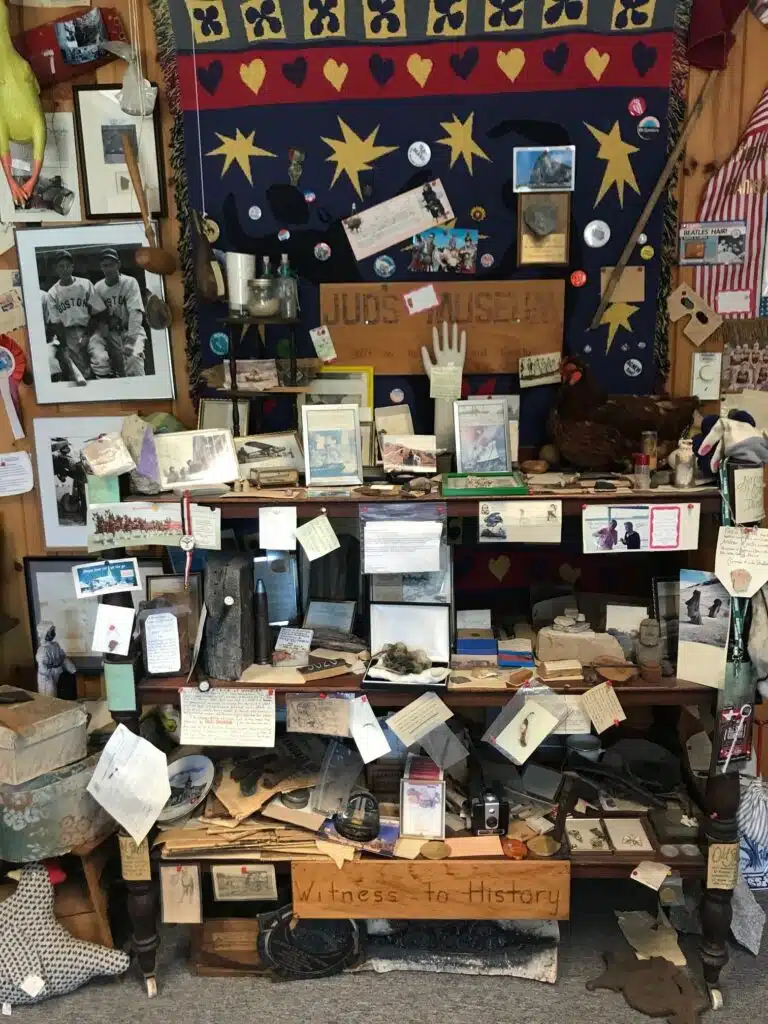 A cluttered display of historic memorabilia, photos, and artifacts in a small museum setting.
