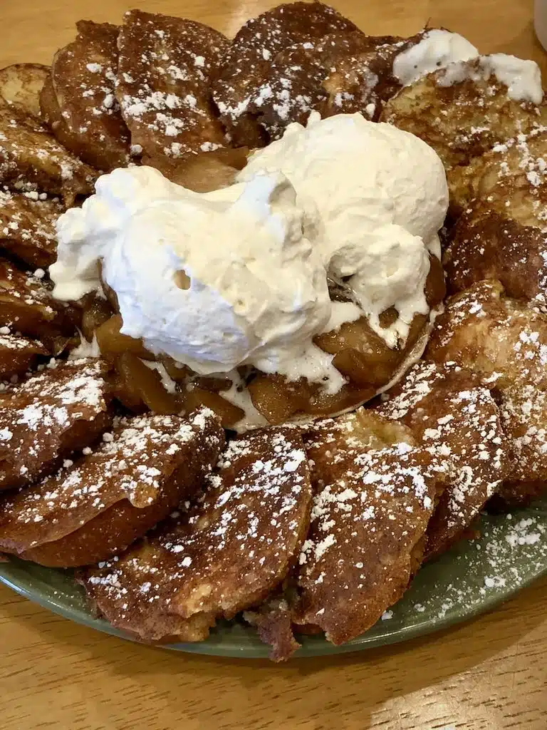 French toast topped with apple compote, whipped cream, and powdered sugar on a green plate.