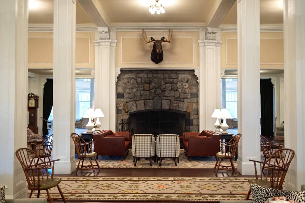 Spacious lounge with armchairs, sofas, stone fireplace, and moose head mounted above the mantel.