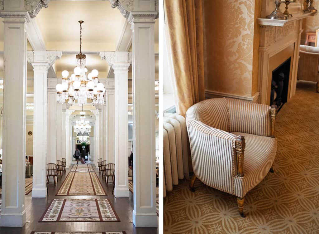 Elegant hotel interior with chandeliers, columns, and patterned carpet; striped armchair near fireplace.
