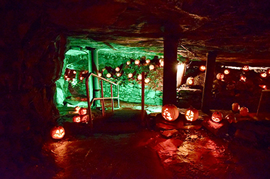 Underground cave decorated with glowing carved pumpkins and green lighting, creating a spooky Halloween atmosphere.