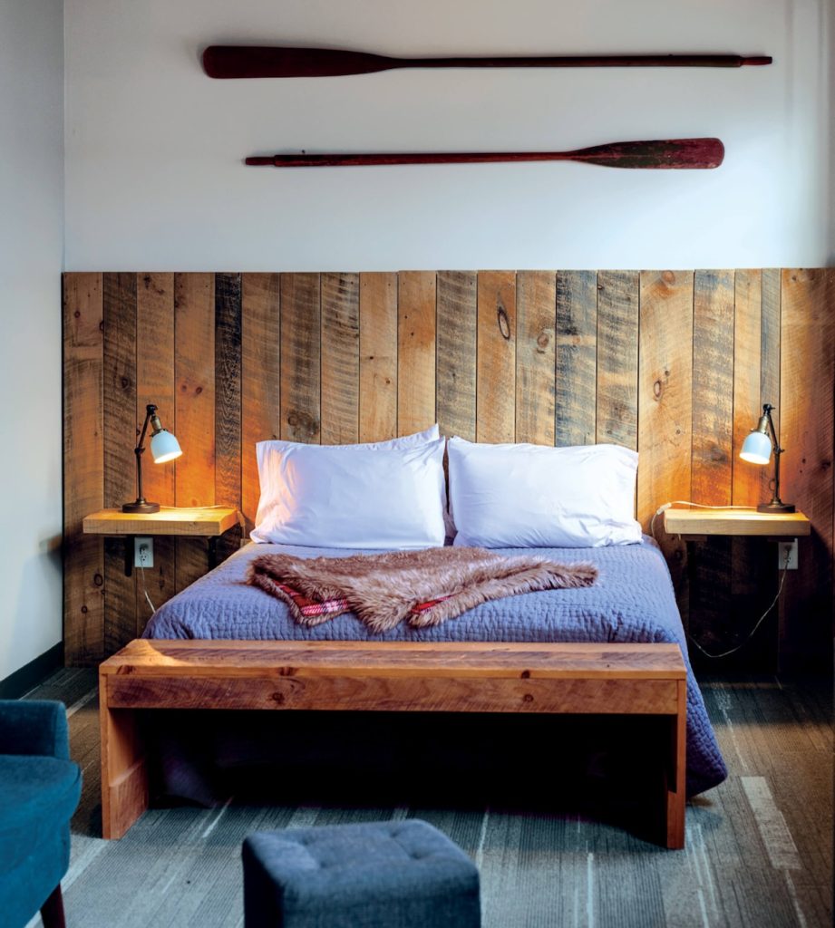 Cozy bedroom with wood-paneled wall, bed, two lamps, bench, and oars hanging above the headboard.