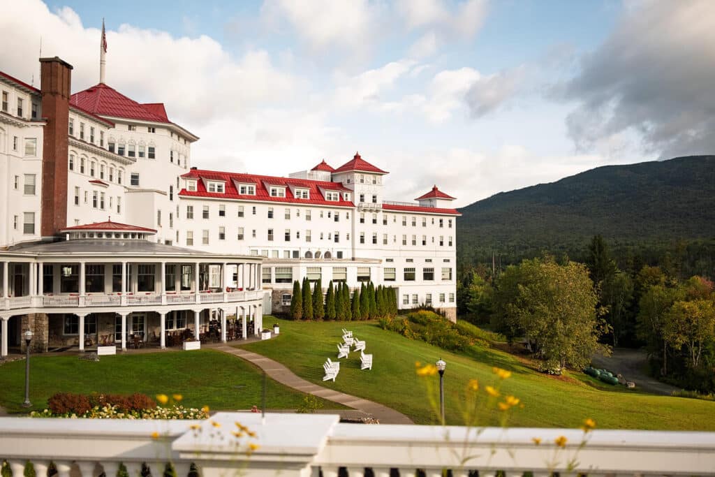 Step in Time: A New Look for the Historic Mount Washington Hotel. Large white hotel with red roofs, green lawn, and mountain backdrop under a partly cloudy sky.