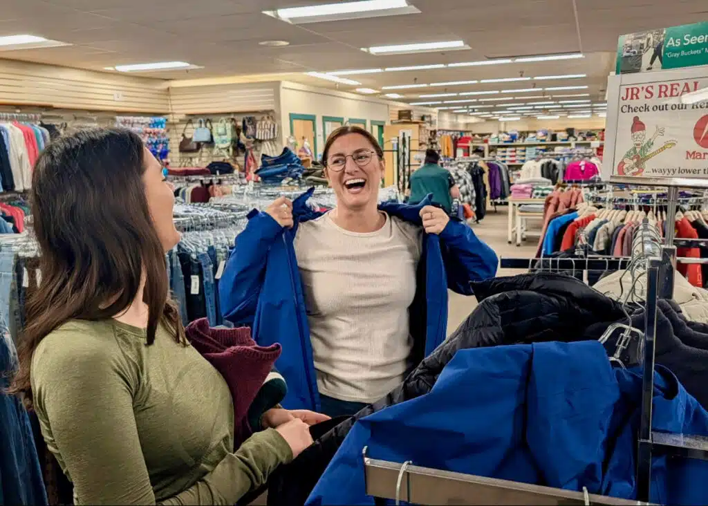 Two women smile and laugh while trying on famous-name jackets at Renys.