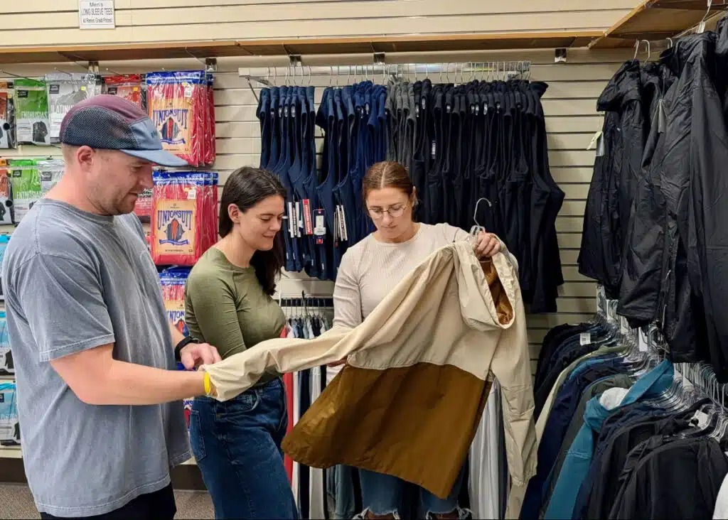 Three people examine a beige and brown jacket at the Renys store in Saco, Maine.