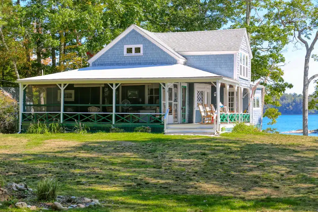 Maine vacation rental - Light blue lakeside house with a screened porch, white trim, and green lawn surrounded by trees.