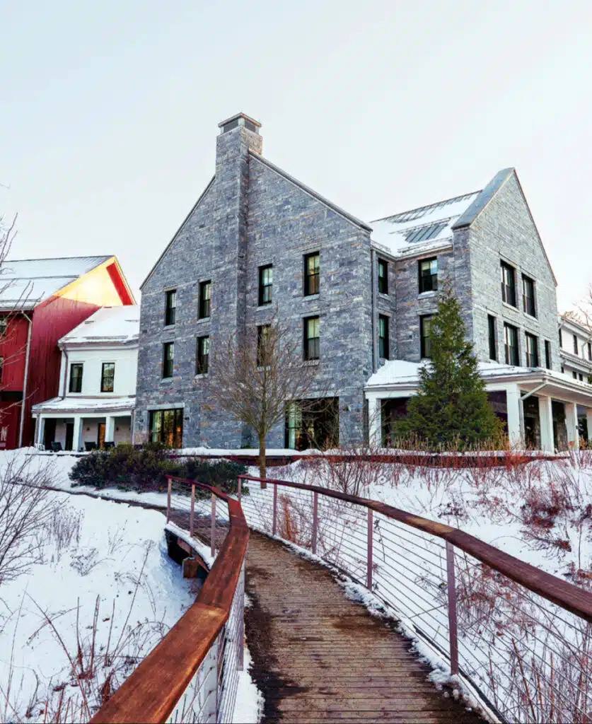 The Williams Inn stone building with snow on the ground, viewed from a wooden footbridge on a winter day.