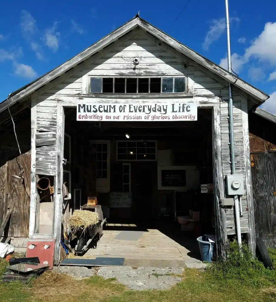 Weathered wooden building with a sign reading “Museum of Everyday Life” on a sunny day.