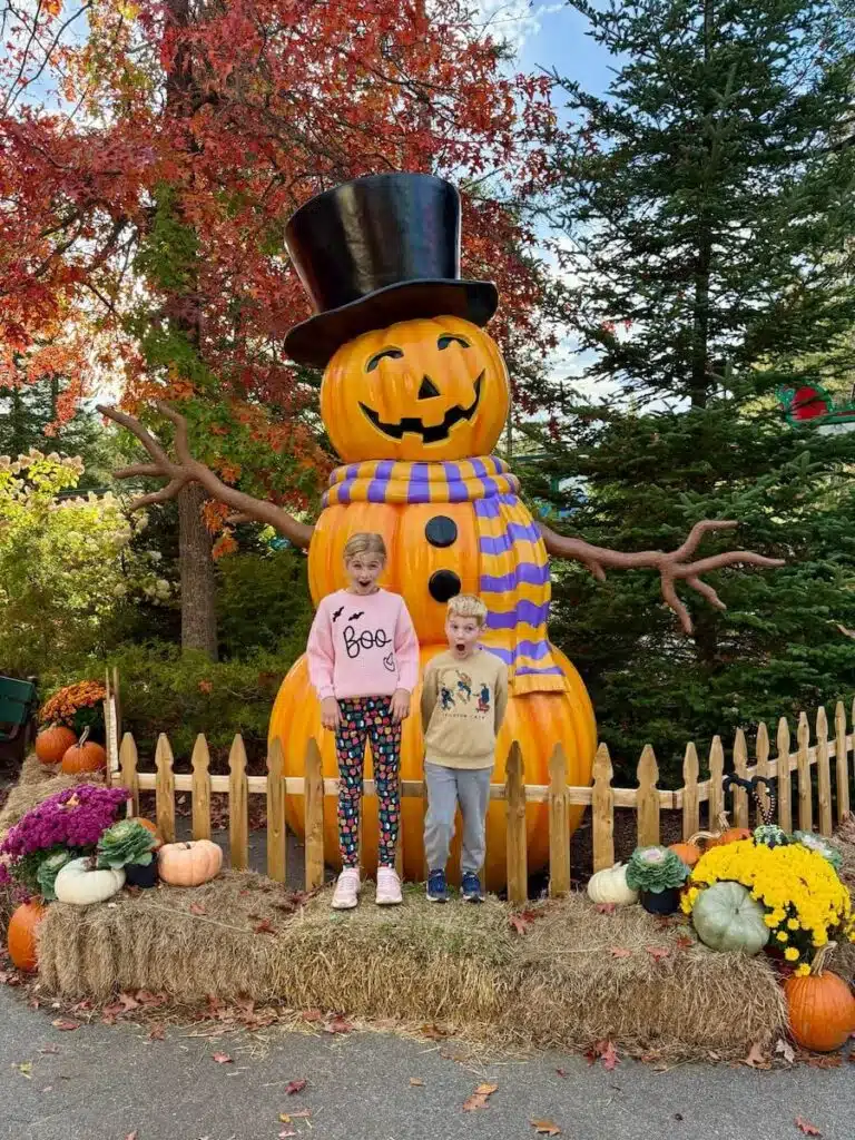 Two children standing in front of a giant pumpkin snowman decoration.