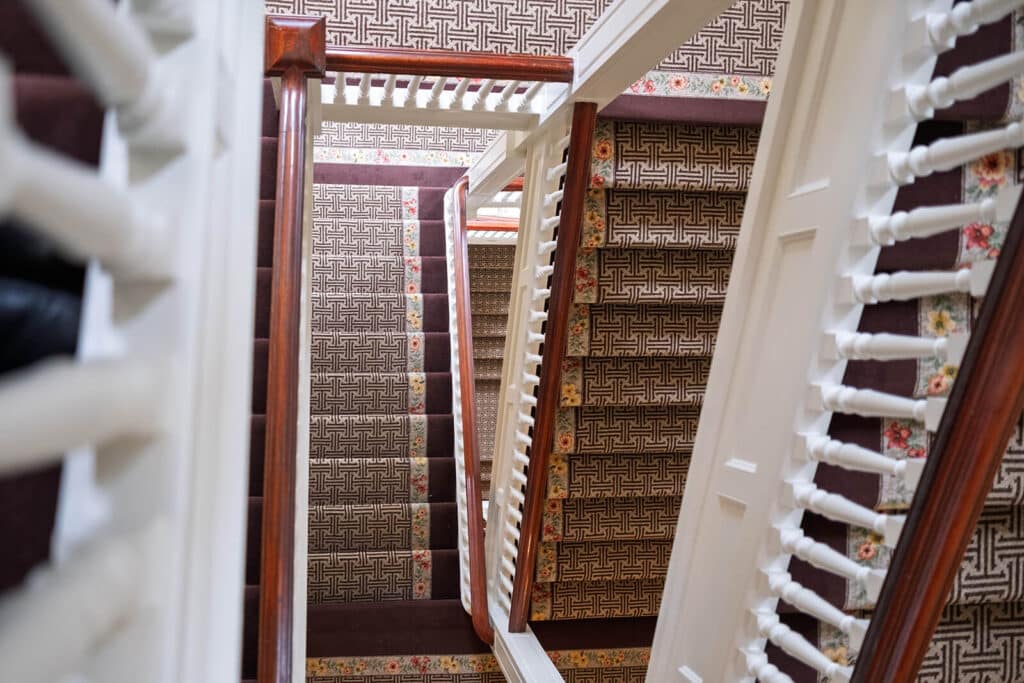 View looking down a switchback staircase with patterned carpet and white railings.