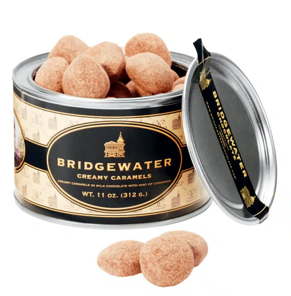 A tin of Bridgewater creamy cinnamon-dusted milk chocolate caramels with the lid off and three candies in front.