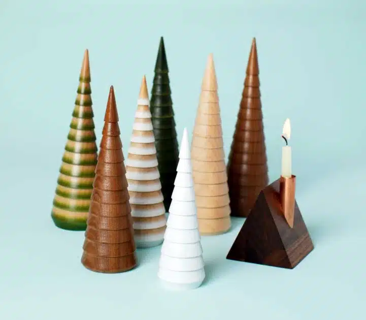 Group of wooden cone-shaped holiday trees and a triangular wooden candle holder with a lit candle.