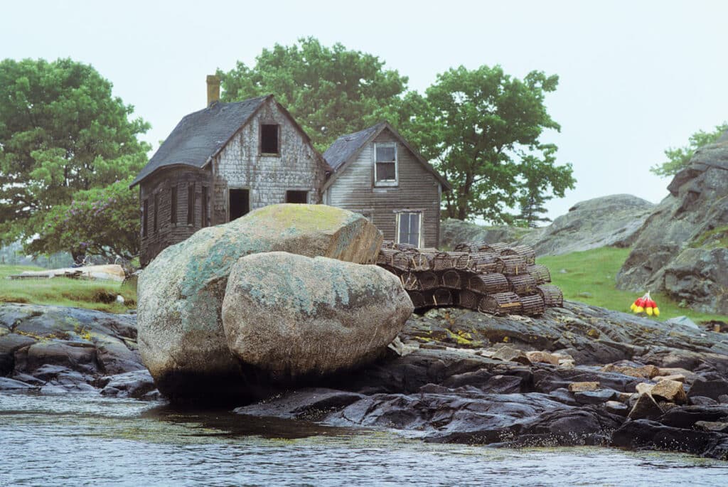 Old houses and a stack of lobster traps on a rocky shoreline.