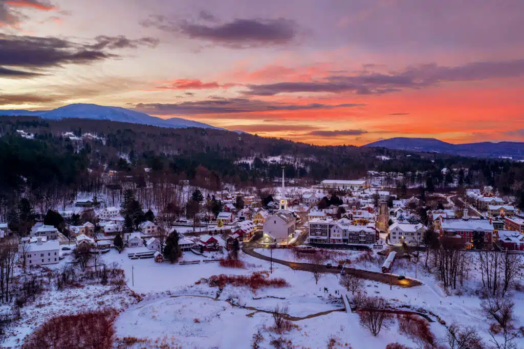 Aerial view of a snow-covered town at sunset with mountains in the background.