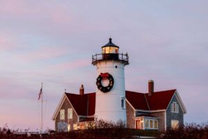 A white lighthouse with a Christmas wreath hanging on the tower during a sunset.