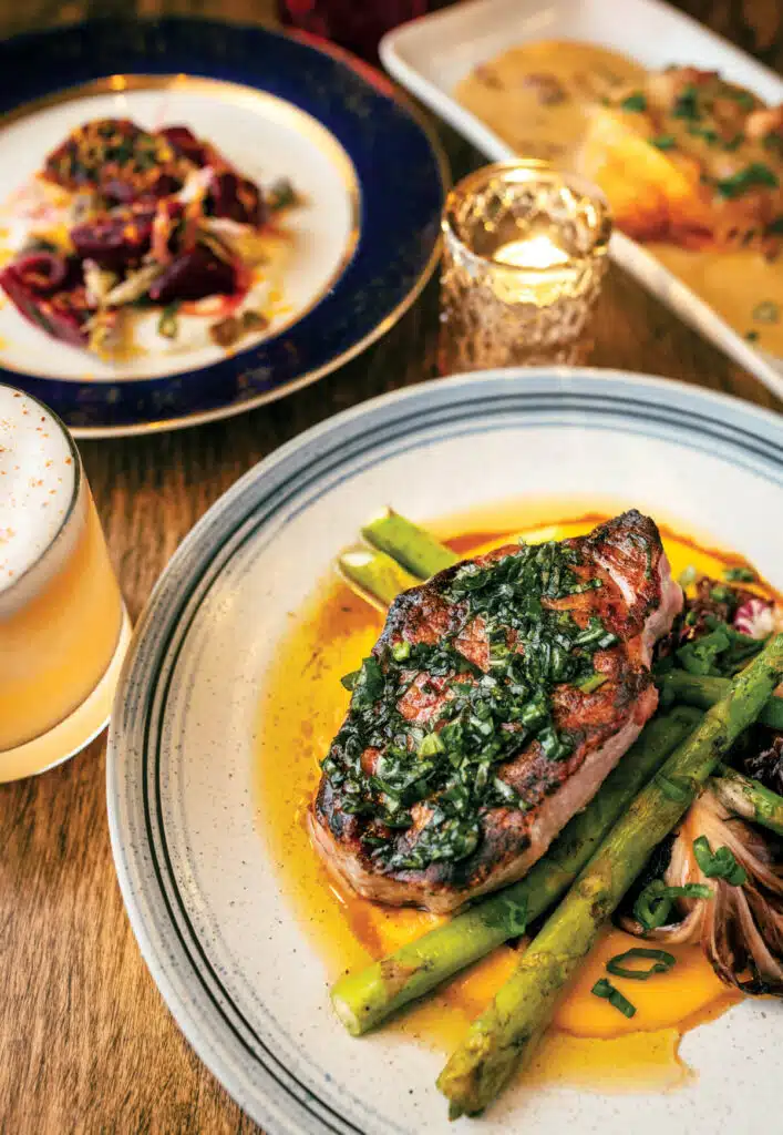 A plate featuring a seared pork chop topped with herbs, served with roasted asparagus.