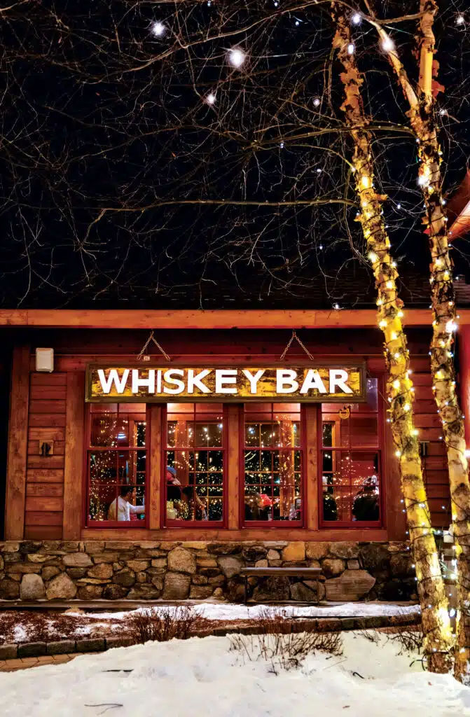 Exterior of a Whiskey Bar at night with a glowing sign and string lights on nearby trees.
