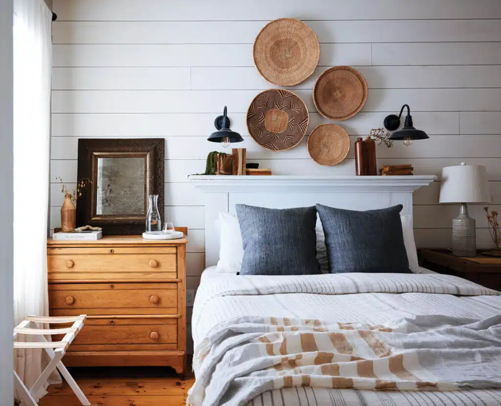 Bedroom with a wooden dresser, bed with blue pillows and striped linens, and woven baskets hanging on the wall.