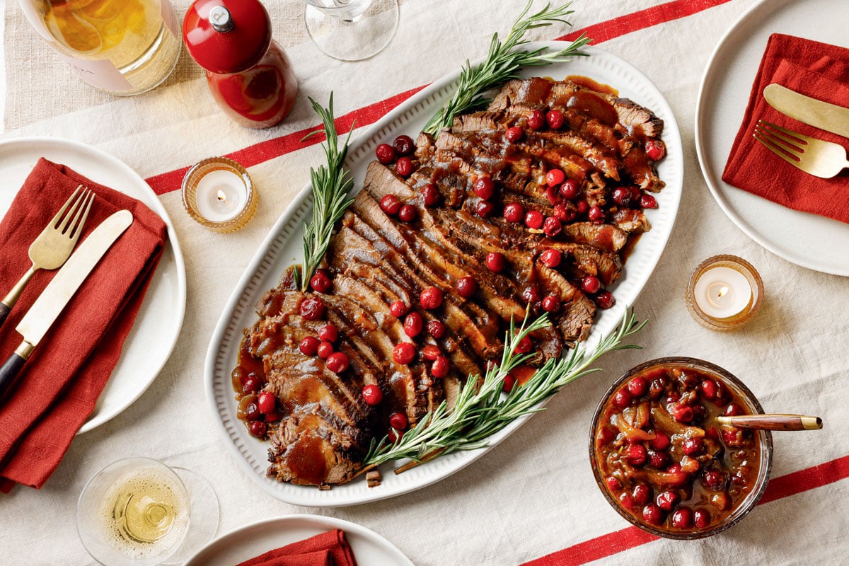Braised Cranberry-Rosemary Brisket. Sliced brisket topped with cranberry glaze and fresh rosemary on a serving platter.