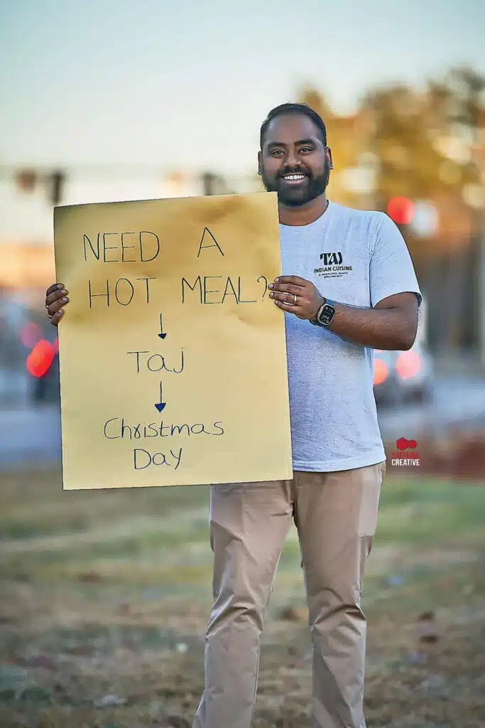 A man holding a sign that reads: “Need a hot meal? Taj, Christmas Day.”