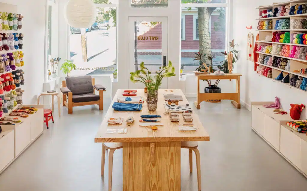 A bright yarn shop with shelves of colorful yarn and a display table with craft supplies.