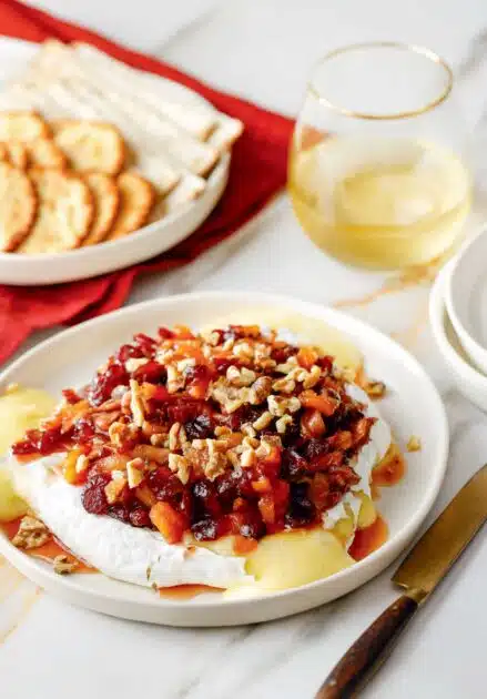 Baked Brie with Spiced Fruit Compote. Baked brie topped with dried fruit and walnuts, served with a plate of crackers and a glass of wine.
