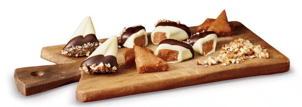 Chocolate-dipped nut candies and pieces of brittle on a wooden serving board.
