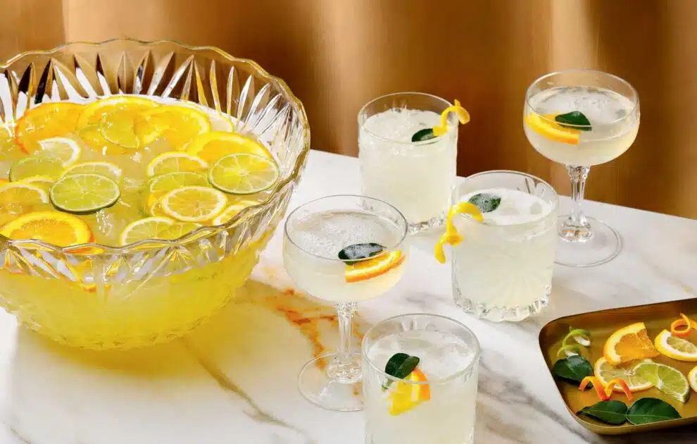 French 75 Punch. A crystal punch bowl filled with citrus punch next to several glasses of the same drink garnished with fruit slices.