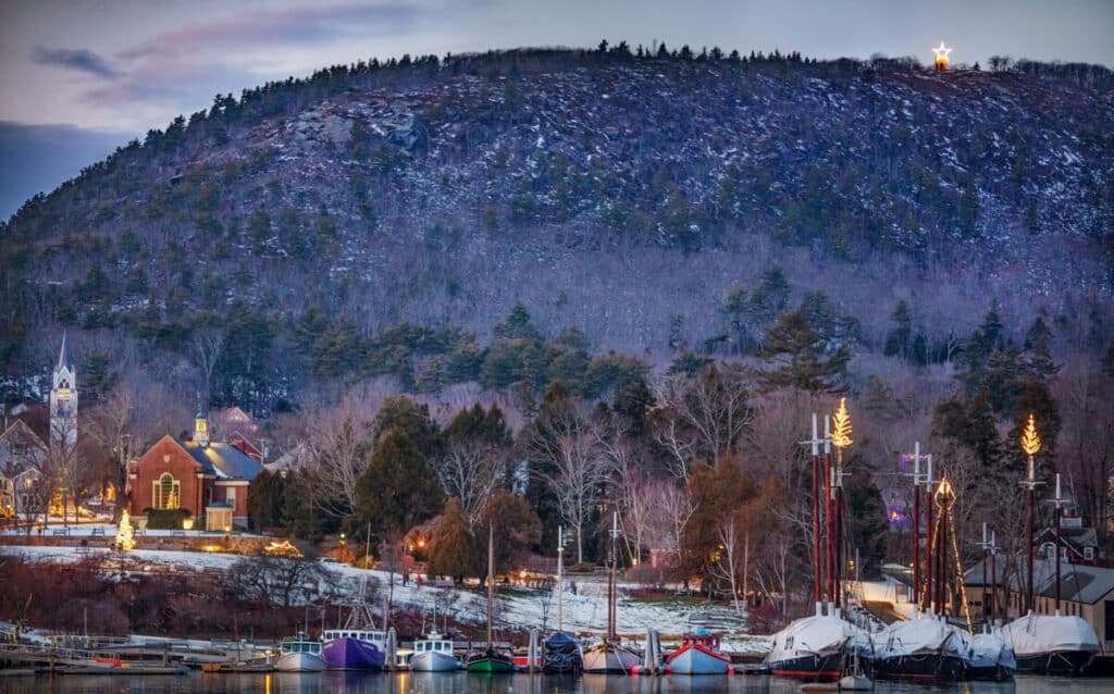 Boats docked in a harbor at dusk with a hilltop illuminated by a lit star.
