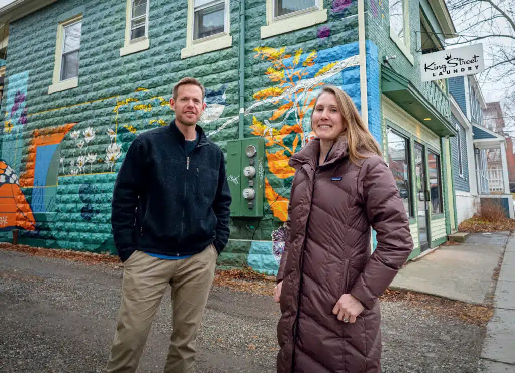 A man and a woman stand outside King Street Laundry in front of a colorful mural.