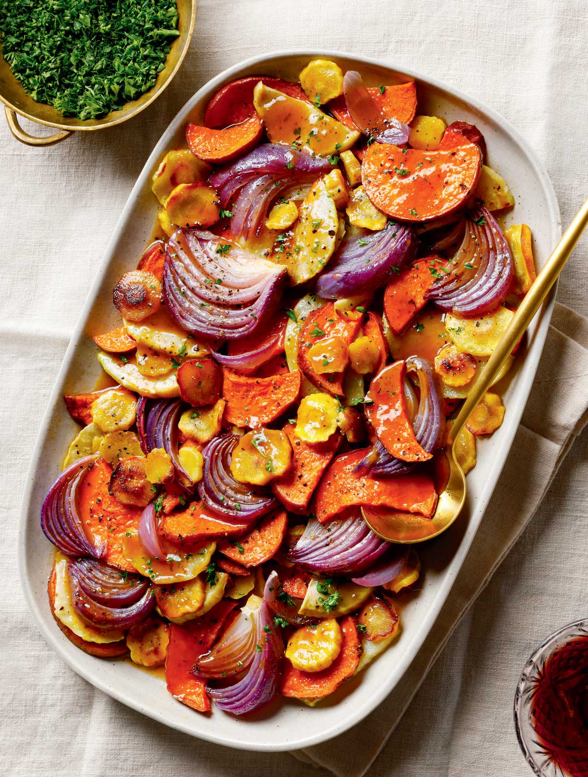 Cider-Glazed Roasted Root Vegetables. Roasted sweet potatoes, yellow carrots, and red onions on a platter with a serving spoon.