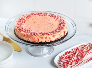 Peppermint cheesecake on a glass pedestal stand with candy canes nearby.