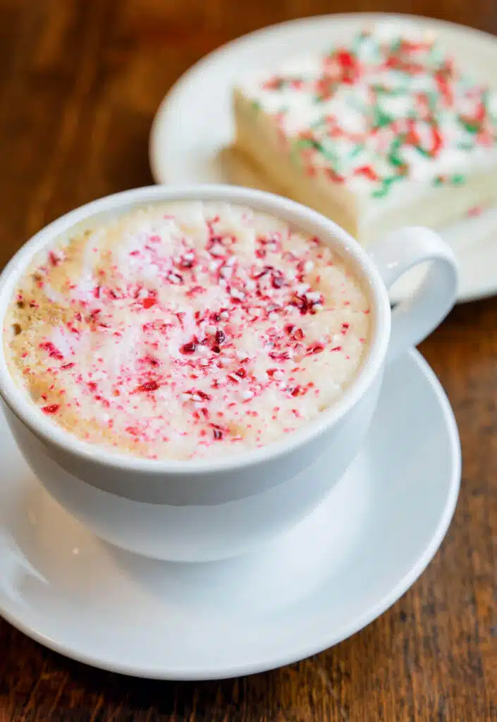 A cup of coffee topped with crushed peppermint next to a frosted cookie with sprinkles.